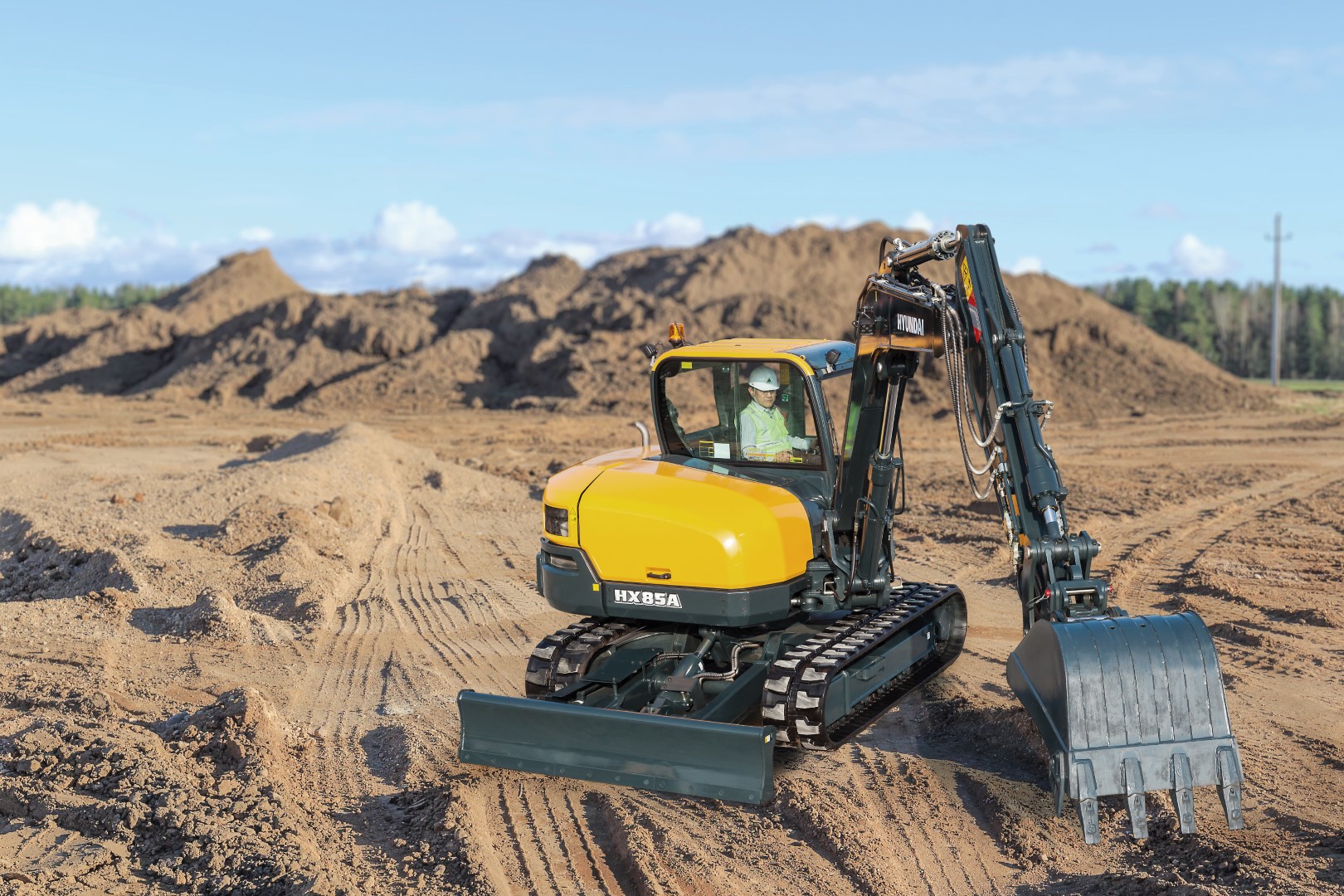 De HX85A compacte graafmachine maakt deel uit van de gloednieuwe A-serie van Hyundai: een nieuwe generatie bouwmachines die voldoet aan de Europese emissiestandaard Euro V. Maar hij heeft nog veel meer in petto! Terwijl aan de regelgeving is voldaan, streeft Hyundai naar een baanbrekend niveau in klanttevredenheid met maximale prestaties en productiviteit, meer veiligheid, meer gemak en een verbeterd uptimemanagement. Deze compact nieuwkomer in de power utility-klasse combineert een robuuste constructie met een uitstekende stabiliteit. Zeer veelzijdig en uitgerust met nieuwe elementen, creëert hij een wereld aan nieuwe mogelijkheden waarin kleine inspanningen bergen verzetten. Het is tijd om het Hyundai-effect te ervaren!